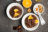 Two bowls of chocolate pudding topped with chocolate-covered orange slices, with walnuts and almonds nearby